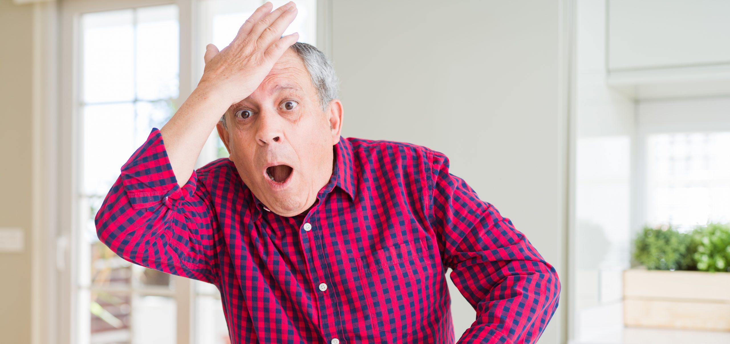 Handsome senior man at home surprised with hand on head for mistake, remember error. Forgot, bad memory concept.