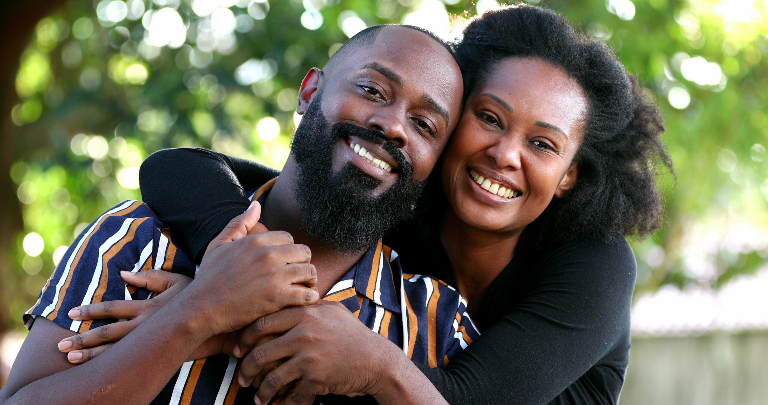 African couple in love embrace and hug outside looking at camera, two romantic couple