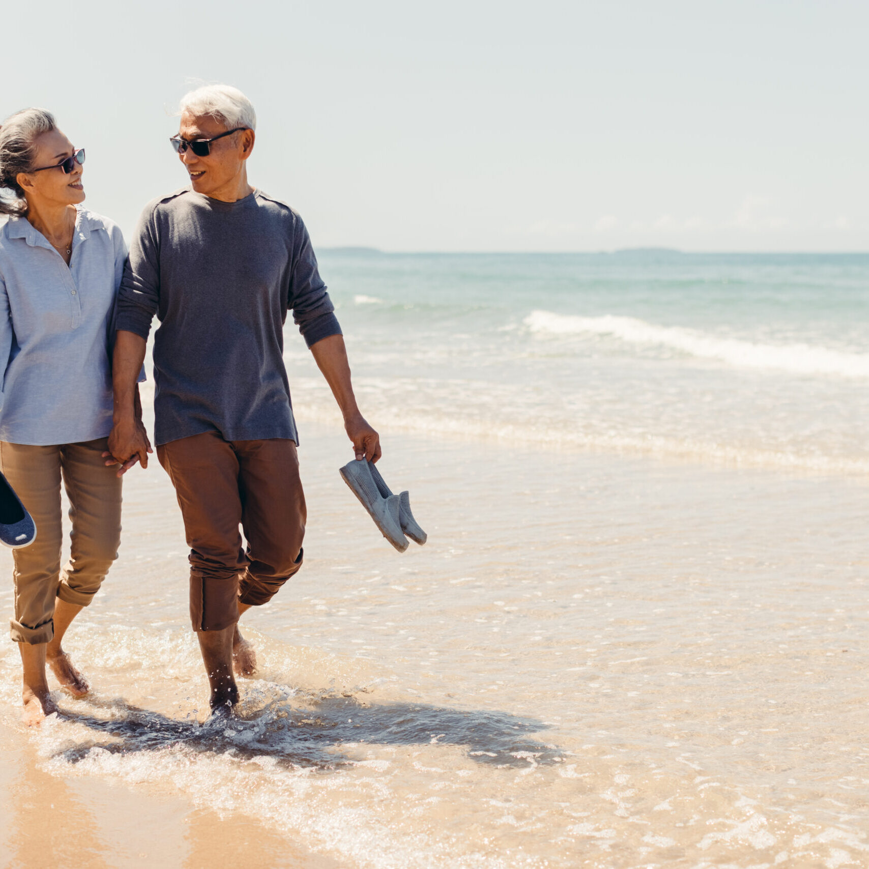 Romantic Senior couple strolling happily along the beach in the sunshine and bright sky. Retirement concept and happy life.